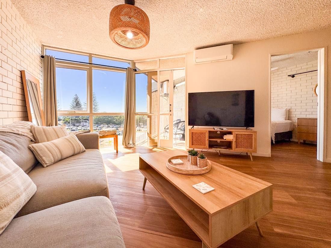 Modern apartment living room with timber floors, opening to an ocean-facing balcony